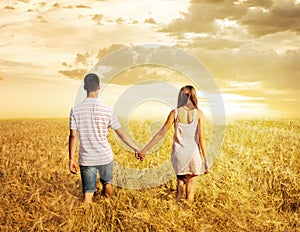 Love couple walking in sunset field holding hands