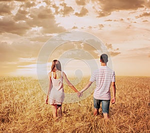 Love couple walking in sunset field holding hands