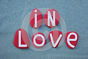 In love, creative slogan composed with red colored stone letters over green sand
