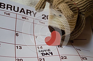 Love day - Paper red hearts marking 14 february Valentines day on white calendar with soft toy puppy