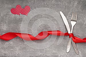 Love dinner silver cutlery. Fork and knife tied with red ribbon on black background, top view