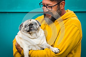 Love dog concept with cheerful adult man hug and hold his own old pug - happy people with animal - colorful yellow and green -