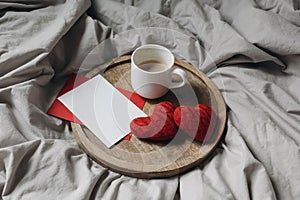 Love, engagement concept. Two red knitted hearts, cup of coffee on wooden plate. Breakfast in bed. Linen duvet cover
