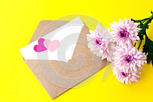 Love envelope with blank letter and pink chrysanthemum flowers with two pink hearts on bright yellow bacground.