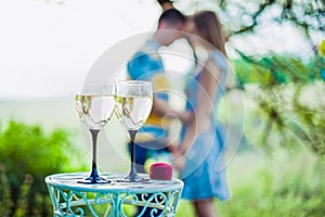 Love, family, anniversary concept - wine glasses and ring box in focus with engaged couple on the background