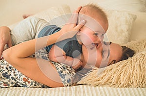 Love and family. Home portrait of a baby boy with mother on the bed. Mom play and kissing her child