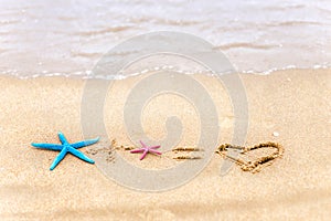 Love formula is drawn on the sand by the sea.Two starfishes Valentine`s Day