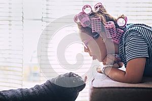 Love in funny moment with woman lay down on the sofa with pink curlers on hair and black lovely pug dog kissing her or making nice