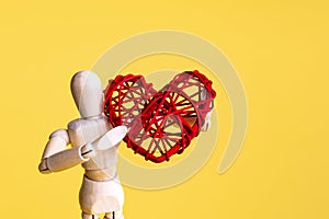 Wooden mannequin holding rattan red heart. Yellow background