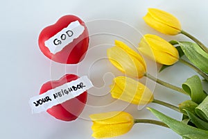 Love God and your neighbor, handwritten text, red hearts, and yellow tulips on white, top view