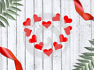 Love greeting composition with frame made red hearts, ribbons and palm leaves on wooden background.