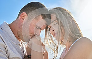 Love, hand and couple kiss at a beach, sharing intimate moment of romance at sunrise against blue sky background. Travel