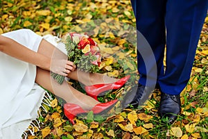 Love and happiness on wedding day. Close up of bride`s and groom`s feet and shoes, colorful bridal bouquet and autumn leaves