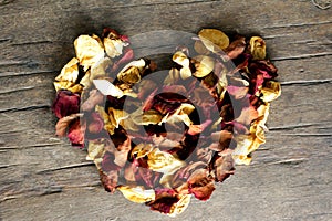 Love heart shape made of dry rose petals on a wooden rustic table background. Christmas and Valentines decoration card concept.