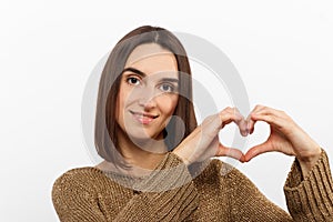 Love, heart shape, peace. Sign, gesture or symbols. Portrait of cute attractive smiling brunette woman, girl shows heart