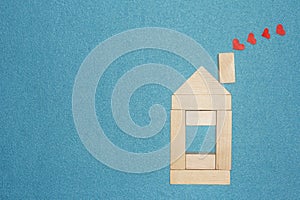 Love in home concept. Wooden house and red hearts from chimney pipe on blue background