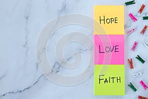 Love, hope, and faith handwritten words on colorful notes with decorative clothespins on white marble background
