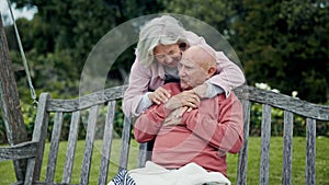Love, hug and old couple on bench in garden, happy morning bonding and relax together in retirement. Marriage, senior