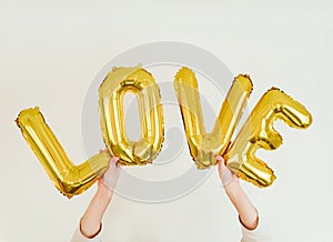 LOVE inscription foil inflatable golden ballon in the hands on the white background. Love, romance and Valentines day concept