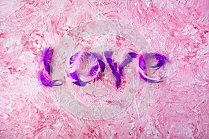 Love inscription made of pink and purple feathers on a textured pink background