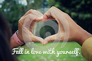 Love inspirational motivational quote - Fall in love with yourself. With hands making love sign against green nature park