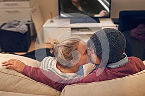 Love, kiss and couple watching tv on a sofa with romance, fun or bonding at home together. Television, movies or people