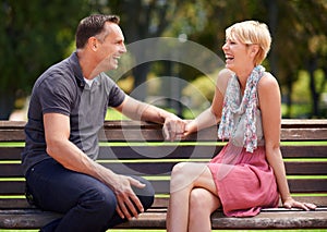 Love, laughing and happy couple on a park bench with funny conversation, gossip or bonding outdoors together. Trust