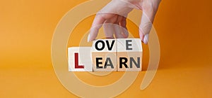 Love and Learn symbol. Businessman hand turns wooden cubes and changes word Learn to Love. Beautiful orange background. Lifestyle