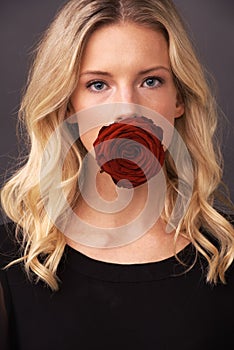 Love leaves her speechless. Conceptual image of a blonde woman with a rose covering her mouth.
