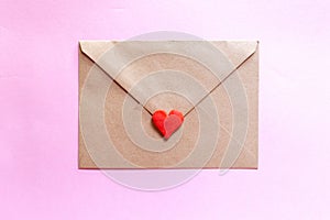 Love letter in a craft envelope with clay red heart on pink background
