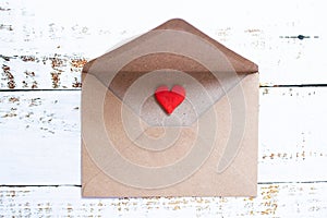 Love letter in a craft envelope with clay red heart on white wood background