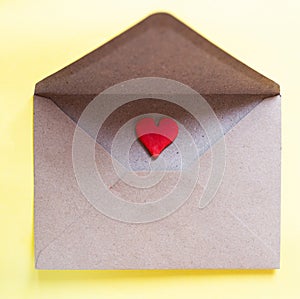 Love letter in a craft envelope with clay red heart on yellow background