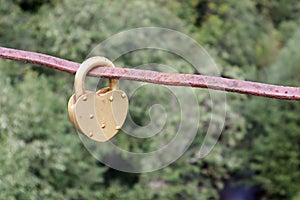 Love lock padlock on the rusty railing of the bridge with green forest on the background