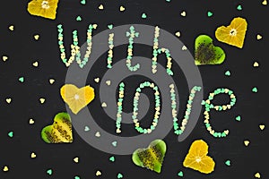 `With love` made of confetti and kiwi fruit on black background. Love concept. Flat lay, top view