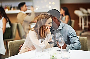 Love, man whisper with woman and in restaurant with wine glasses, happiness or cheerful on Valentines day. Romance