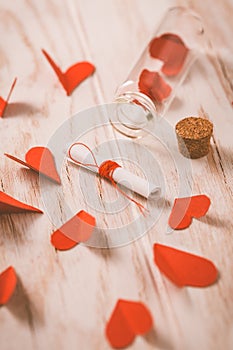 Love message in a bottle with paper hearts on wooden background