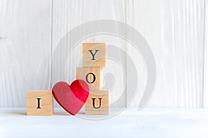 Love message written in wooden blocks with red heart, white wood background.