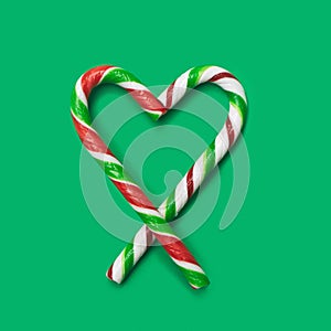 Love minimal concept. Flat lay arrangement heart shape made of two different candy canes against green background