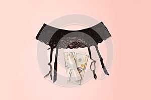 Love for money concept. Sexy black belt underwear with grease and dollars banknotes on pink background