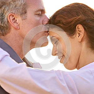 The love of my life. A mature man kissing his lovers forehead against a bright sky.