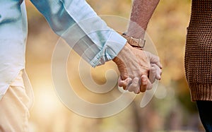 Love, nature and senior couple holding hands while walking in autumn park, forest or woods for retirement leisure