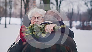 Love at old ages. Elderly couple hugging in the park. Woman holding red roses