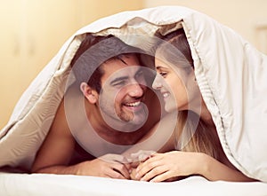 Love the one youre with. Shot of a loving young couple smiling at each other while lying under a blanket together.