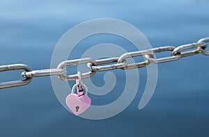 Love padlocks in pink hanging on metal chain fence