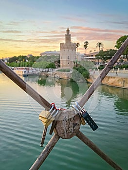 Love padlocks on Seville bridge with Golden Tower Torre del Oro and the guadalquivir river in the background at sunset photo