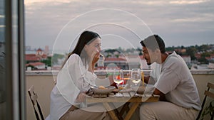 Love pair enjoying food at balcony with sunset city view. Couple celebrating