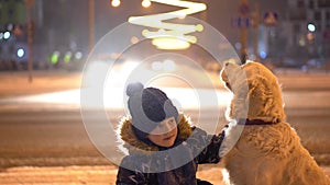 Love for pets. little boy stroking his dog outdoors in winter in the evening city