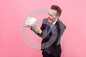 Love for pets. Portrait of cheerful handsome man holding cute white rabbit on his hand. isolated on pink background