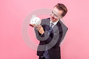 Love for pets. Portrait of pleased happy man looking at white rabbit on his palm and smiling, admiring cute pet. indoor studio