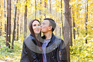 Love, relationship, family and people concept - man kissing his wife in autumn park